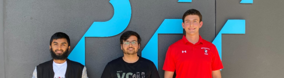 three male student interns standing in front of a company branded wall