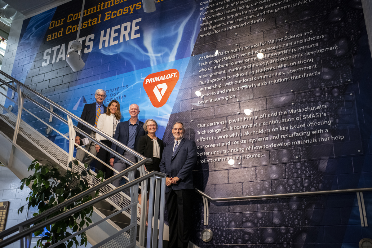 Pat Larkin, Deputy Director, Massachusetts Technology Collaborative, Lieutenant Governor Karyn Polito, Chancellor Mark Fuller, Jean VanderGheynst, Dean of Engineering and interim Dean of SMAST, and Mike Joyce '85, PrimaLoft CEO posing in front of a mural outside the new lab