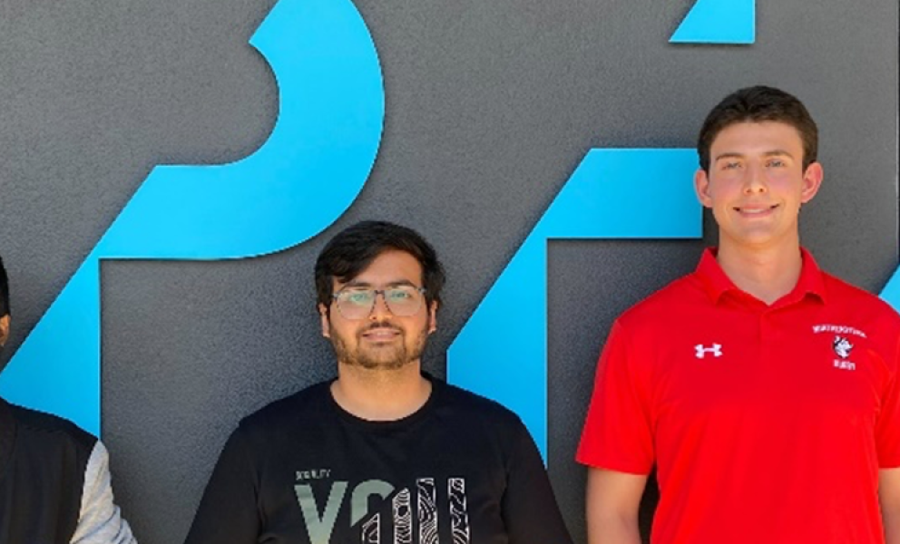 three male student interns standing in front of a company branded wall