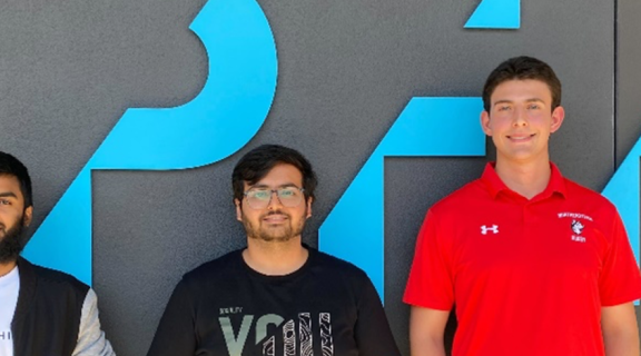 three male student interns standing in front of a company branded wall